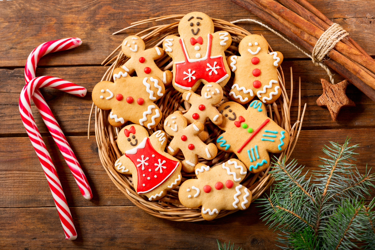 decorated gingerbread cookies on a wicker platter with candy canes, cinnamon and a Spruce sprig as decoration