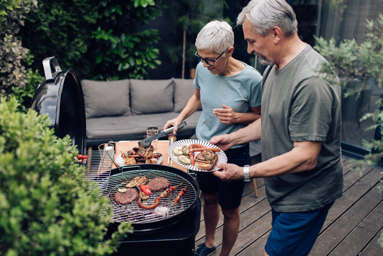 Senior couple preparing barbecue for the whole family in the backyard on a charcoal grill. 