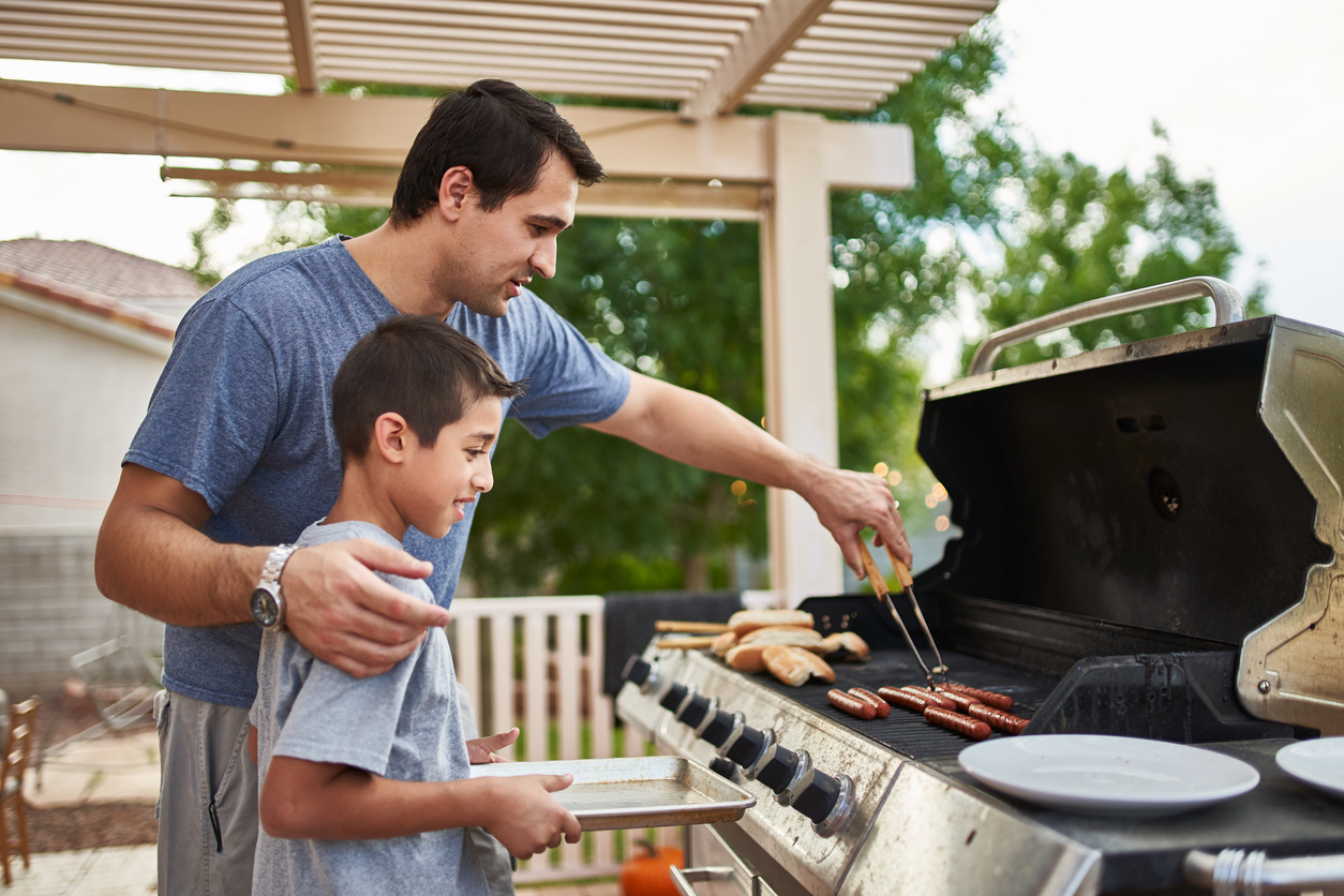 Father teaching son how to grill hot dogs on a gas grill. 