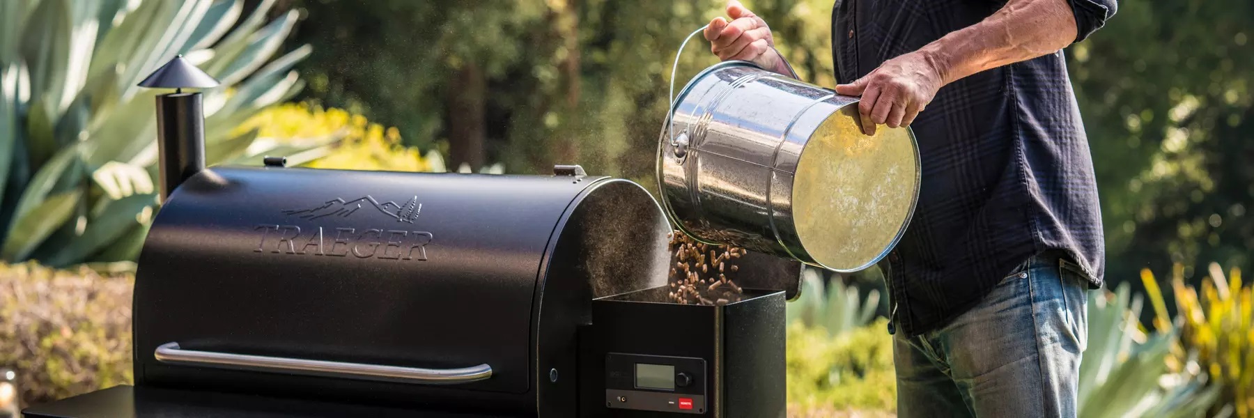 Man pouring a bucket of Traeger pellets into a Traeger outdoor grill.