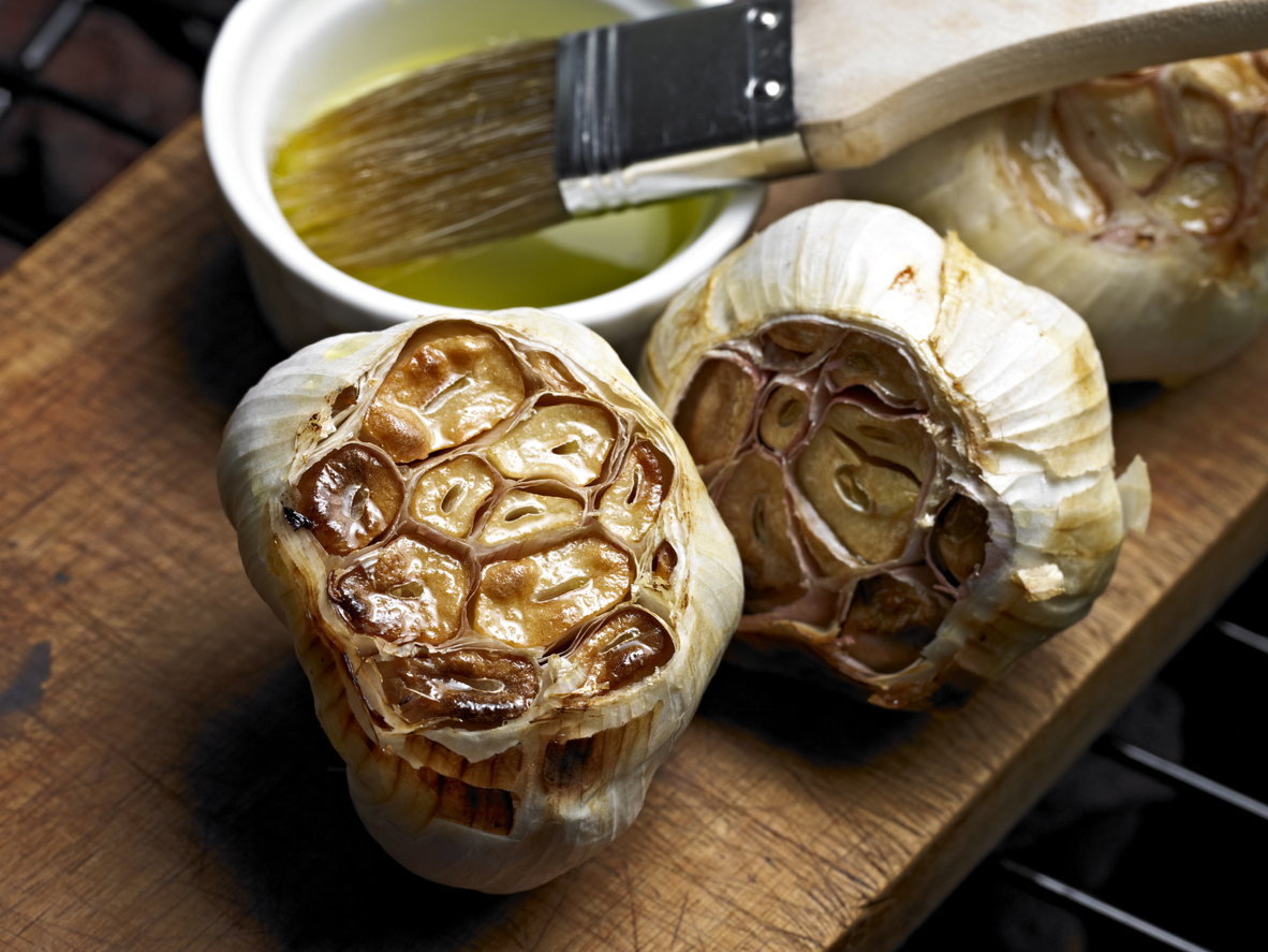 oven roasted garlic heads on a wooden platter with olive oil and pastry brush