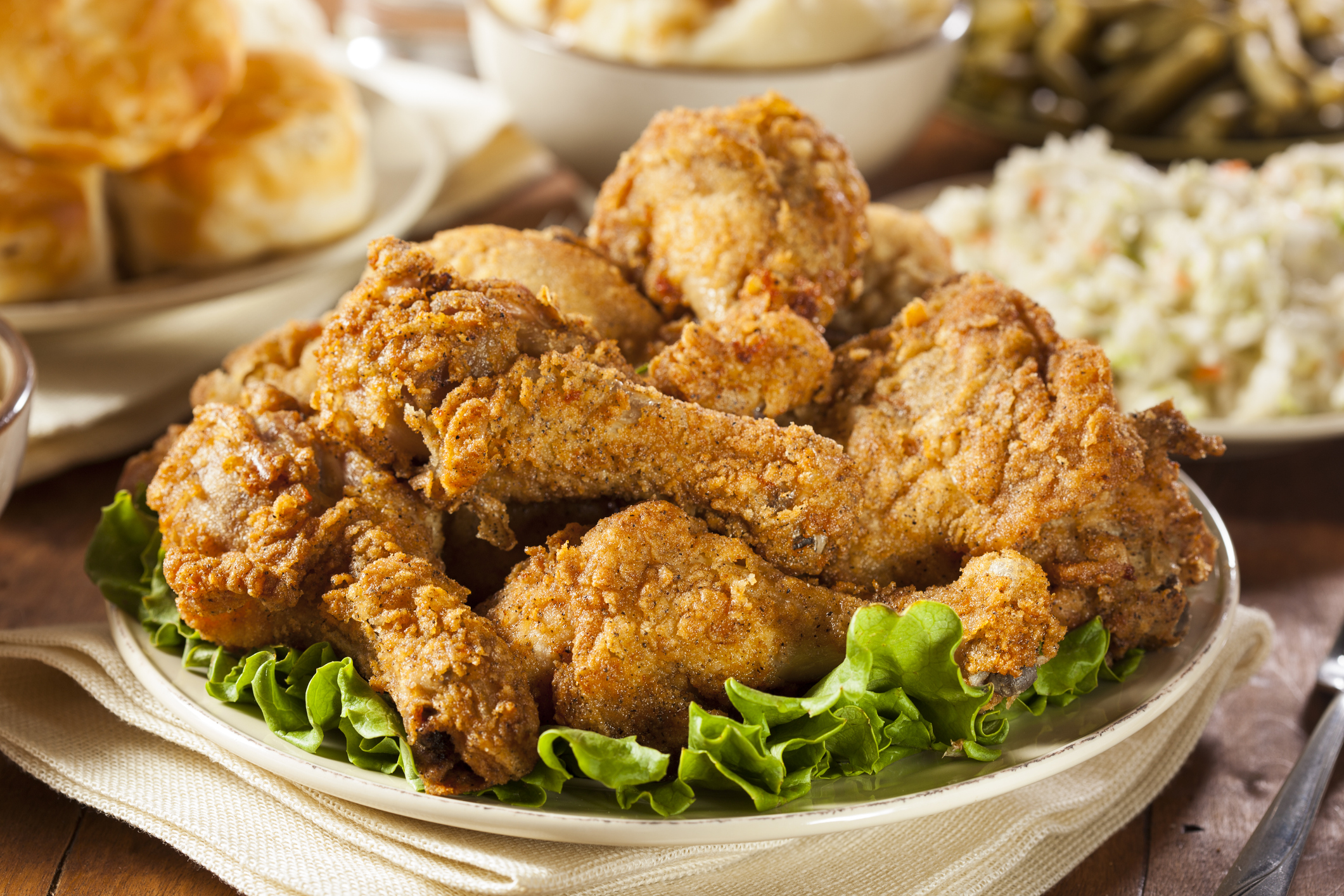 Shot of fried chicken on a platter of lettuce in the forefront with servings in the background