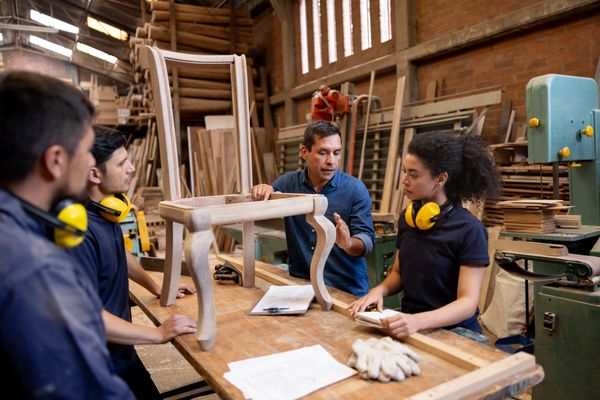 A craftsman demonstrating how to carve a chair to students 