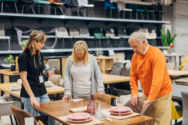 iStock Credit: Kosamtu A mature couple inspects a dining room set along with a saleswoman