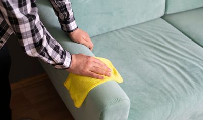A person cleaning a green microfiber sofa 
