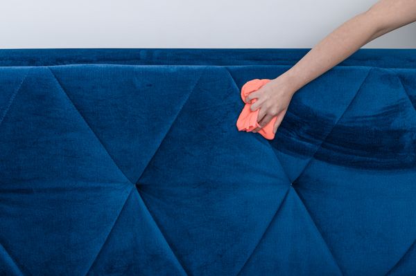 A person cleaning a blue microfiber sofa with a pink rag 
