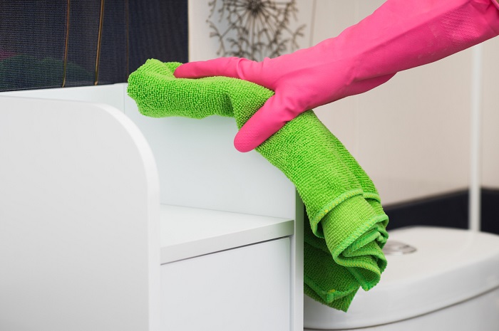 Hand with rubber glove wiping down furniture with microfiber cloth.