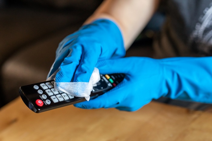 Pair of hands with rubber gloves wiping down remote control.
