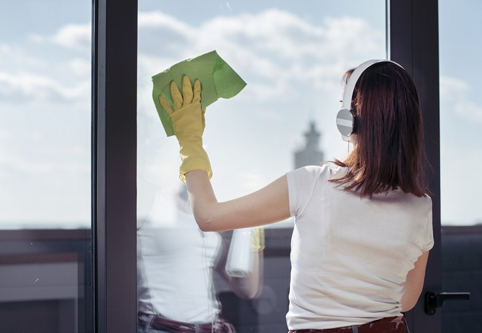 Woman wearing headphones washing window with rubber gloves and microfiber towel.