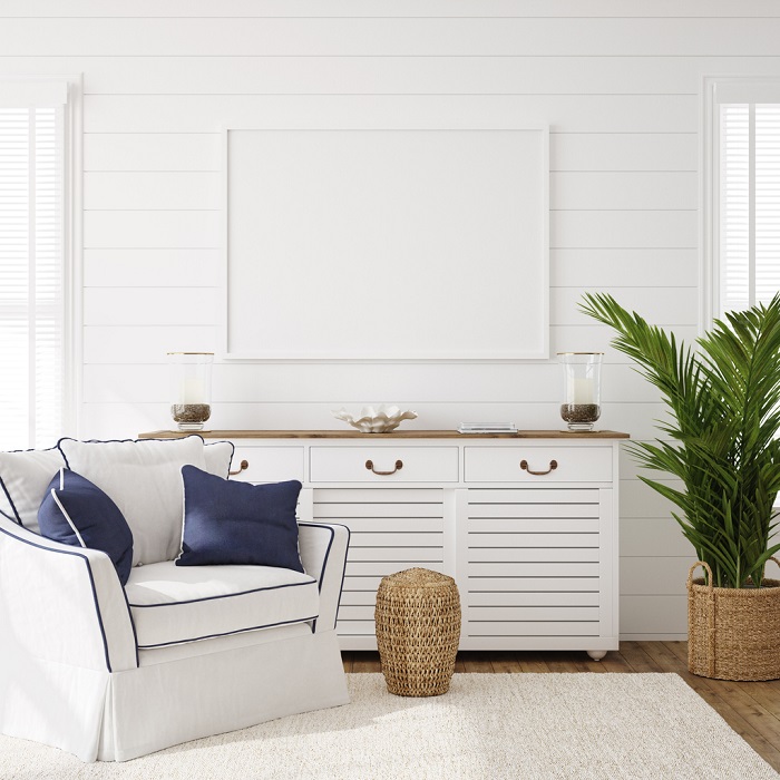 Coastal style living room with white chair and blue and white pillows, with a palm plant in the corner. 