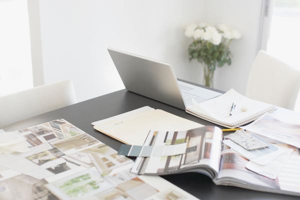 A table featuring a laptop, notepad, and several designer magazines 