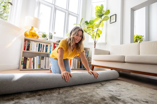 A woman rolling out a rug in a living room 