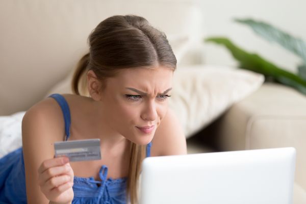 A woman holding a credit card looking bewildered at a laptop 