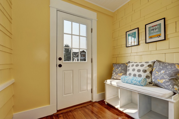 Entryway with yellow walls and storage bench in white with colorful pillows. 