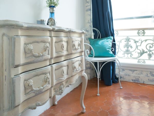 A close-up of a white French provincial dresser and chair with décor 