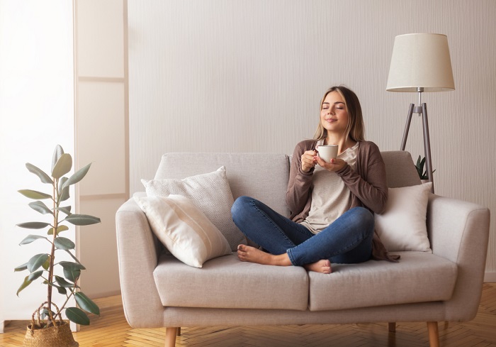 Young woman sniffing hot drink while sitting cross legged on a couch. 