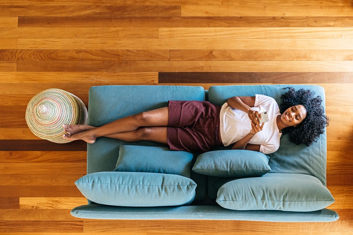 Woman resting on blue sofa and smiling while scrolling on mobile phone.