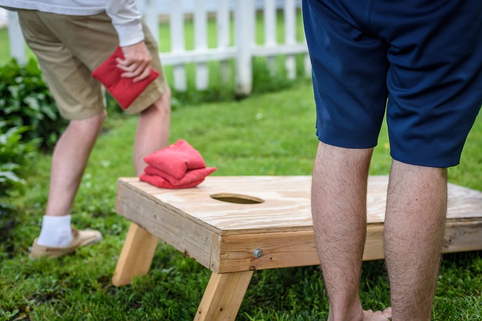 Lower half of two men playing corn hole game in backyard. 