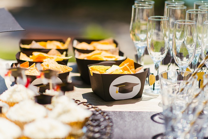 Table with chips, cupcakes, and champagne glasses with a graduation theme. 