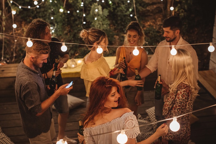 Group of friends having summer party in backyard with focus on string lights. 