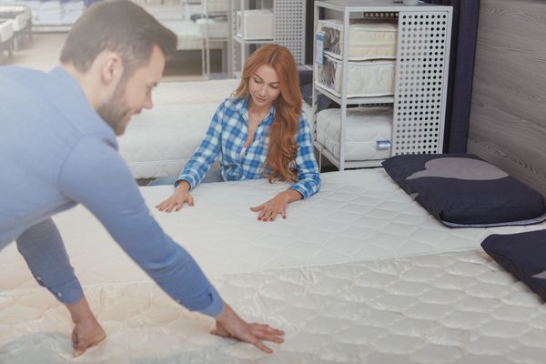 A man and a woman feeling a mattress in a store
