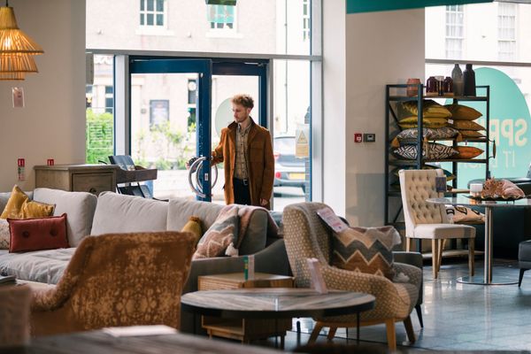 A young man in a brown coat walking into a furniture store 