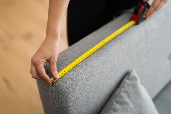A person measuring a sofa with a tape measurer 