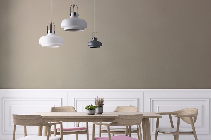 Modern wooden dinner table and chairs with a netrual painted wall in the background and hanging lights. 