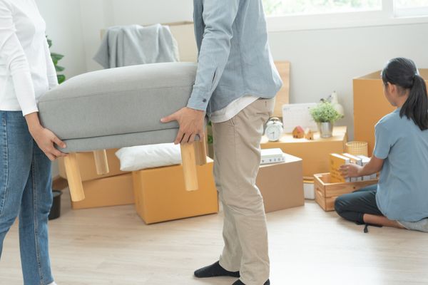 Two people carrying an ottoman while a girl packs in the background 