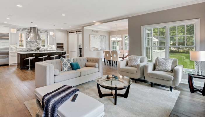 A neutral colored living room with several armchairs and a softa in front of a kitchen.