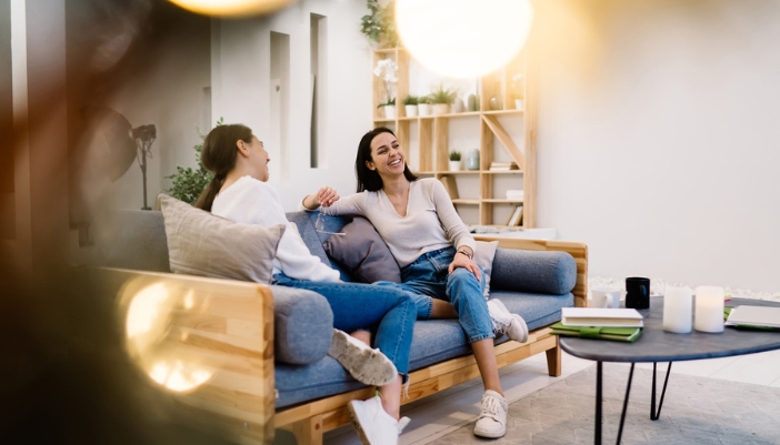 Two friends sit on a couch and happily chat.