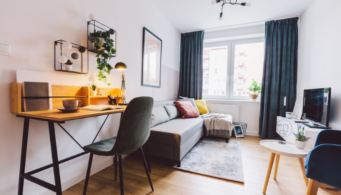 A small living room with an L-shaped couch and a tall work desk. 