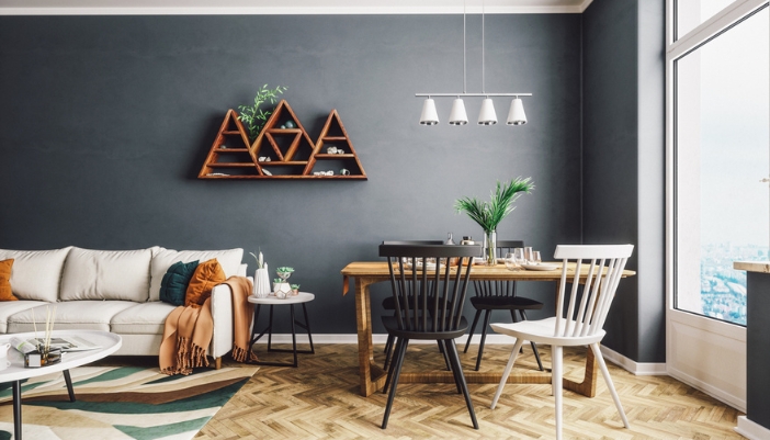 A white couch sits in front of a dark wall and next to a natural dining table.