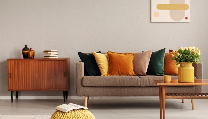 A brown couch with retro inspired colors sits next to a vintage table/bookcase.
