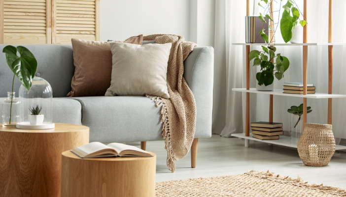 A gray couch with neutral throw pillows and blankets rest next to a wooden bookshelf.