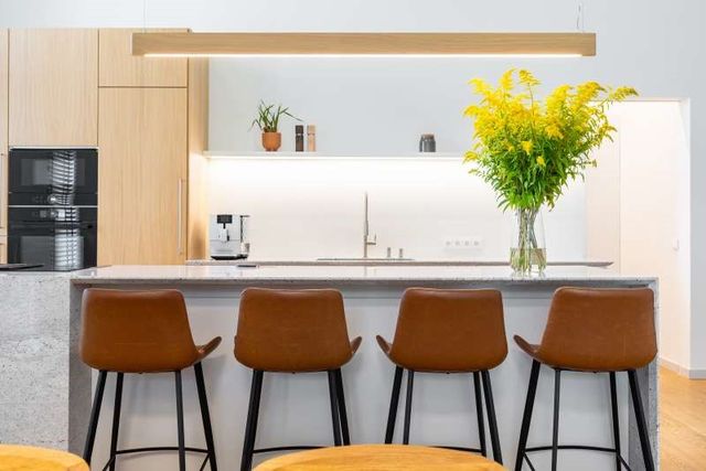 front view of a modern kitchen with light wood and white cabinets in the background, and a white island and four stools in the foreground