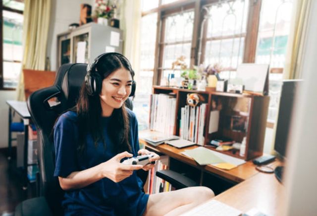front view of a woman sitting on a desk chair playing video games at her desktop computer, with storage solutions in the background