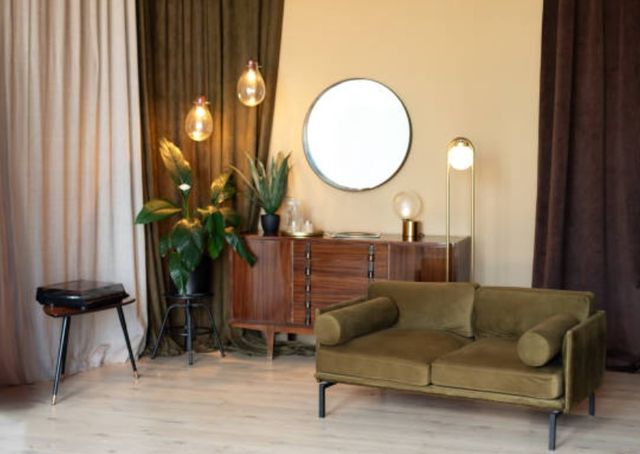front view of the corner of a mid-century modern living room with a sofa, sidebaord, plant, and curtains on either side
