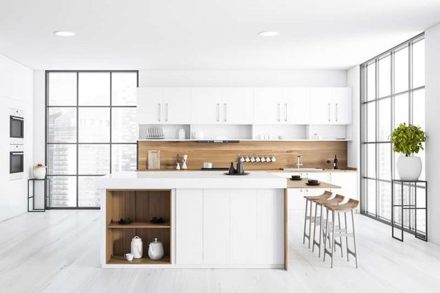 front view of a large all white kitchen with a light wooden backsplash and a white island with three matching stools