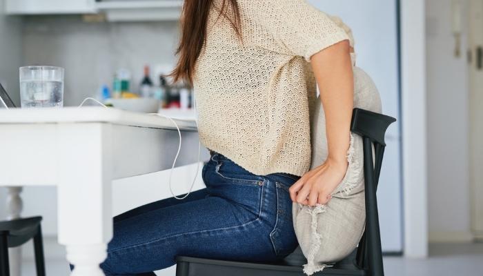 Woman trying to get comfortable with pillow on chair