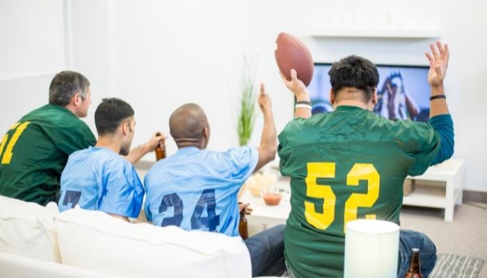 Men wearing jerseys sitting down in all spots to watch TV