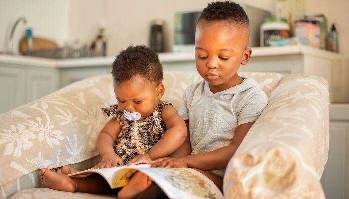 two young kids reading a book on a chair