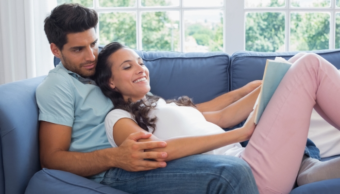 Couple cuddling on sofa reading a book