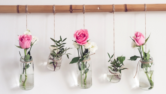 Glass jars repurposed as flower vases hanging from a bamboo shelf