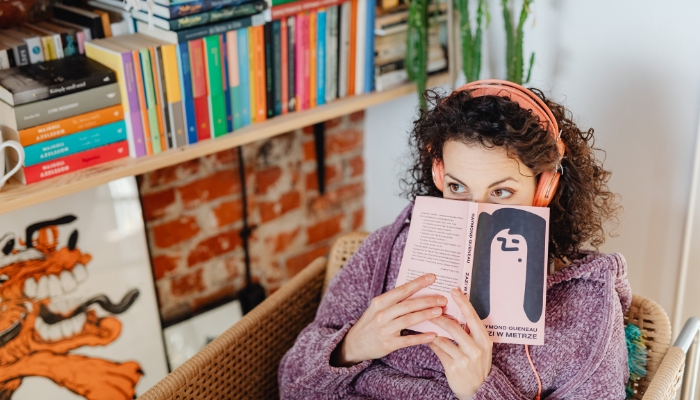 Woman reading novel in front of bookshelves with horizontal stacks
