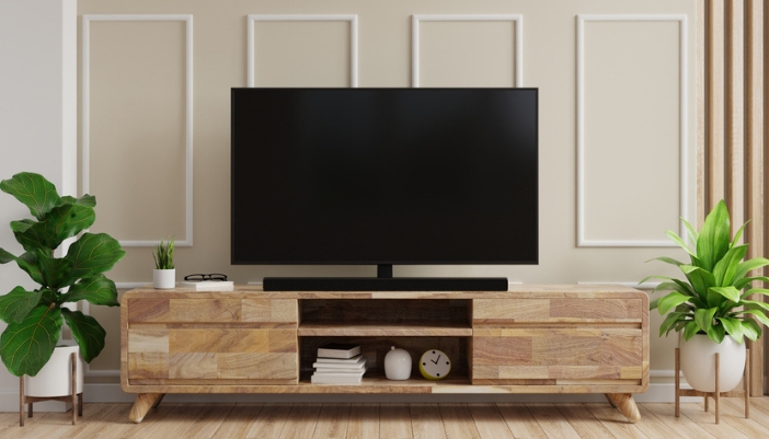 A wooden tv stand with a flat screen TV on top and greenery to the side.