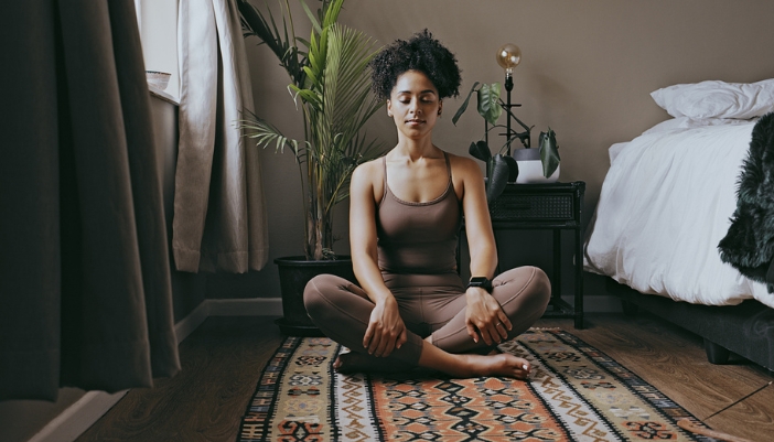 A woman relaxes and meditates on a woven rug in her home.