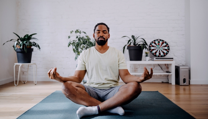 A man meditates in a sparsely decorated room at his home.