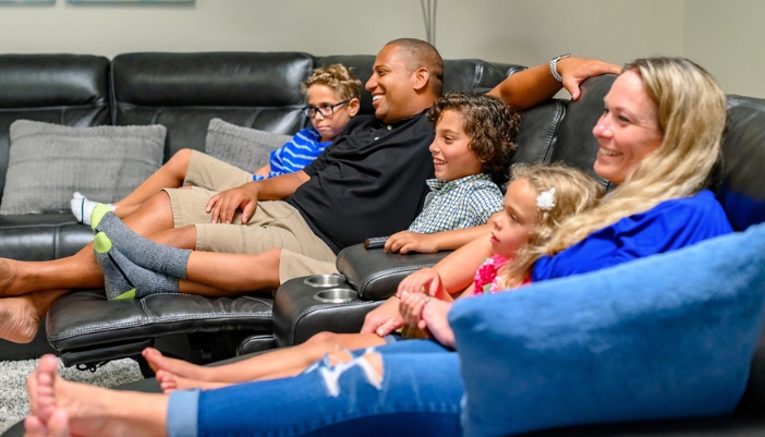 A family sits on a gray leather recliner couch relaxing together.
