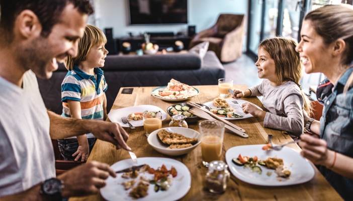 A family sits at a wooden dining table eating pizza slices.